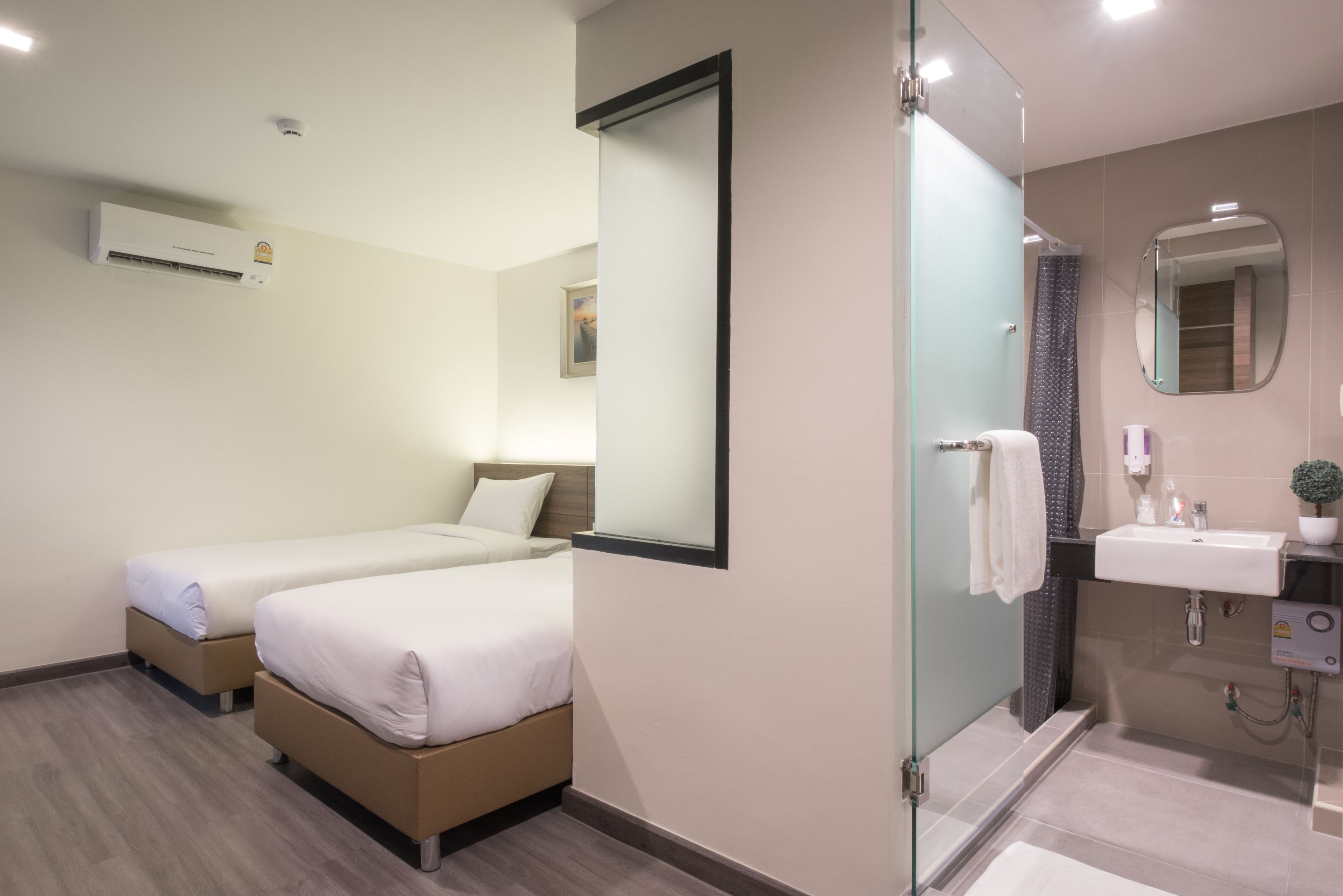 Une chambre d’hôtel moderne équipée de deux lits simples, d’une douche en verre, d’un lavabo et d’un climatiseur fixé au mur.