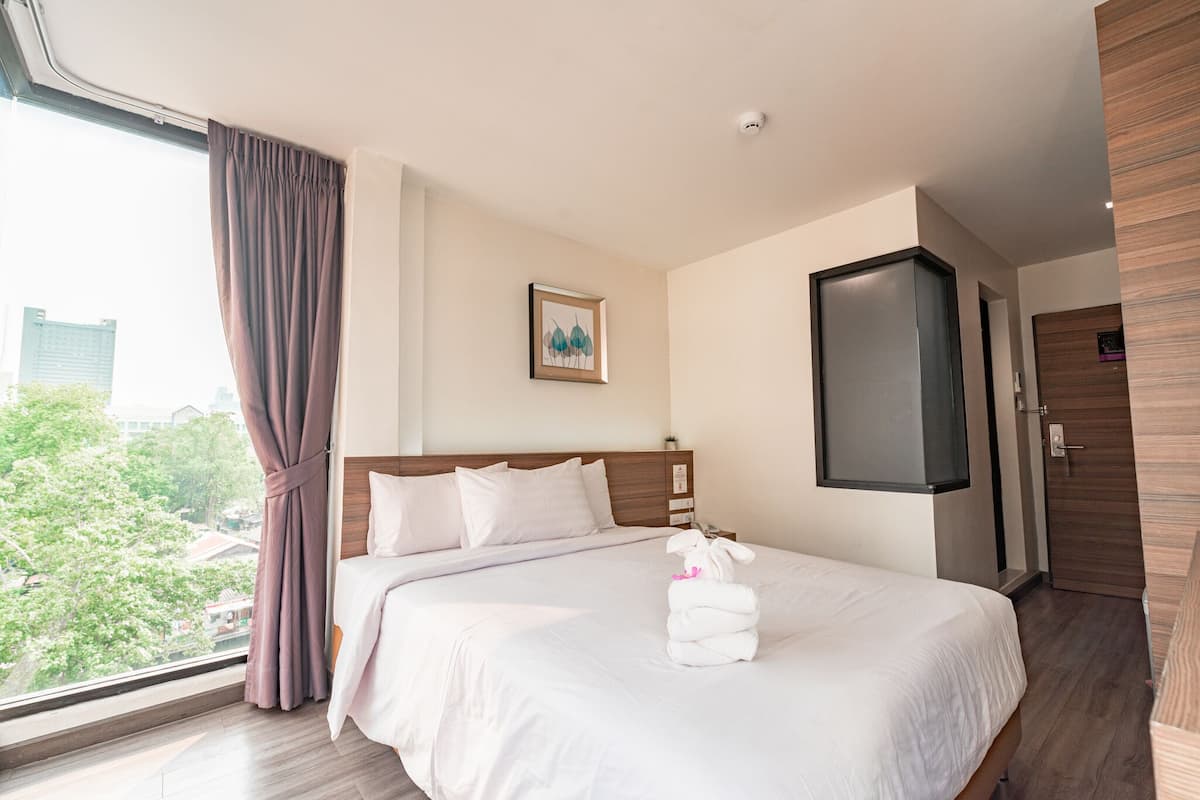 Habitación de hotel con una cama grande, vistas de la ciudad y una puerta con panel de madera.