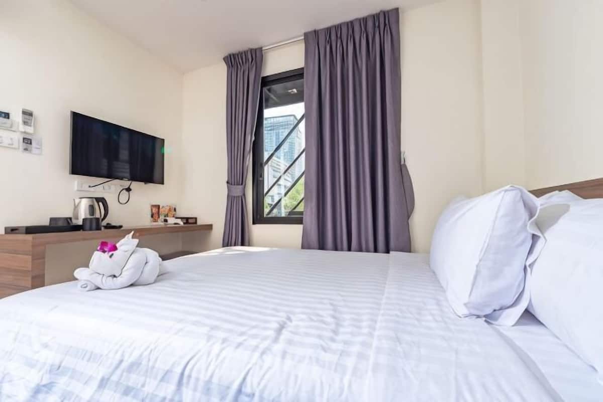 Una habitación de hotel con cama, televisor de pantalla plana, escritorio con cafetera y ventana con cortinas.