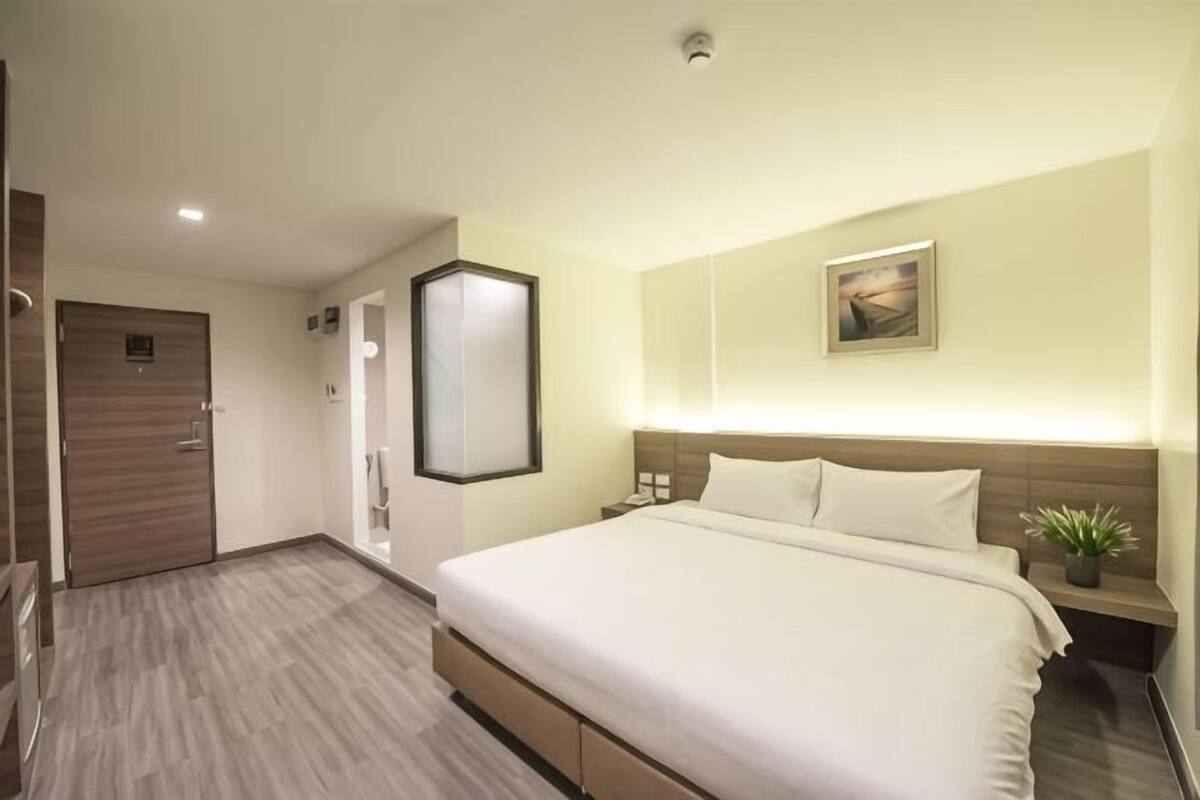 Una habitación de hotel con una cama grande, mesita de noche y un espejo montado en la pared.