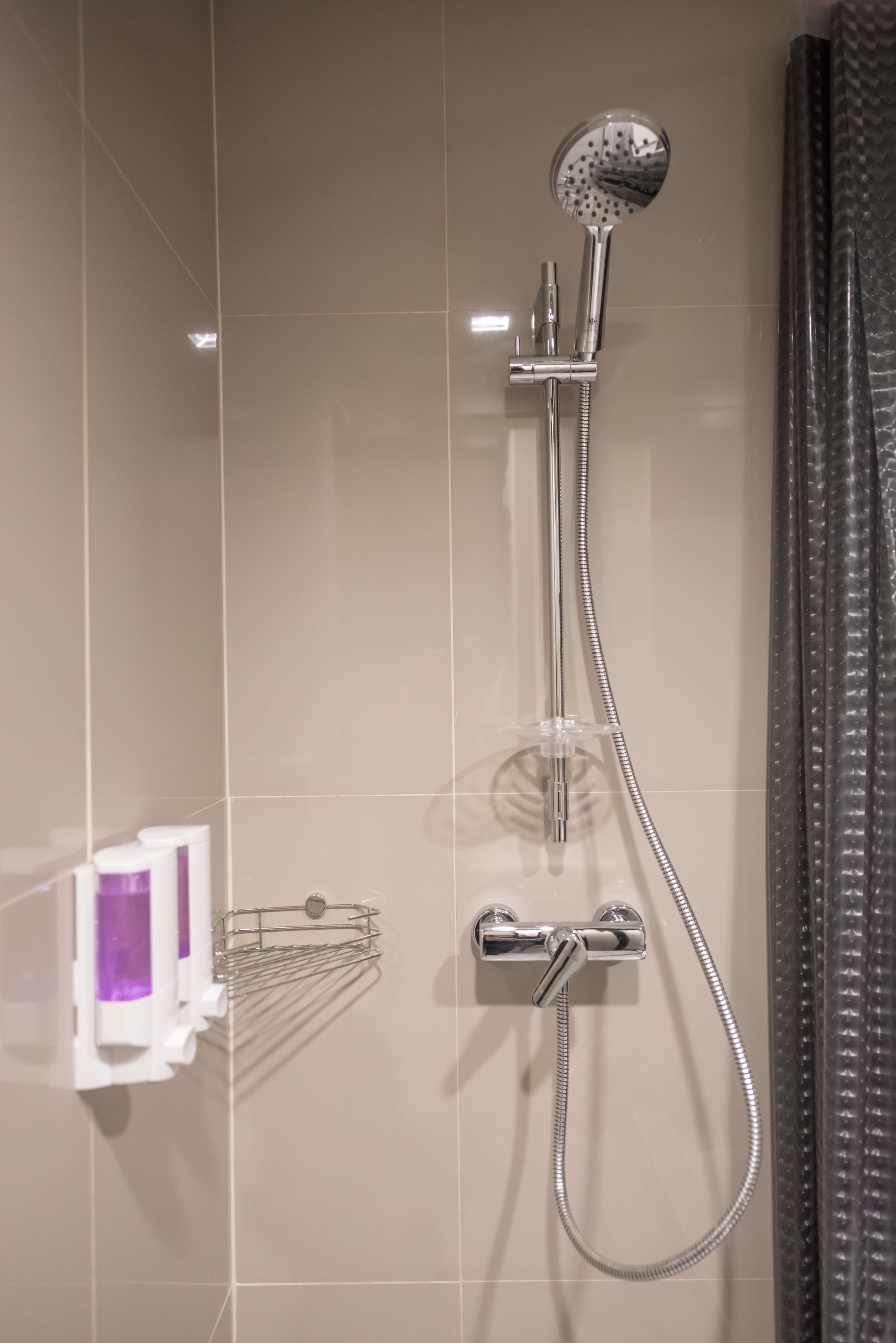 A modern bathroom with a shower, a towel rack, and a soap dispenser.