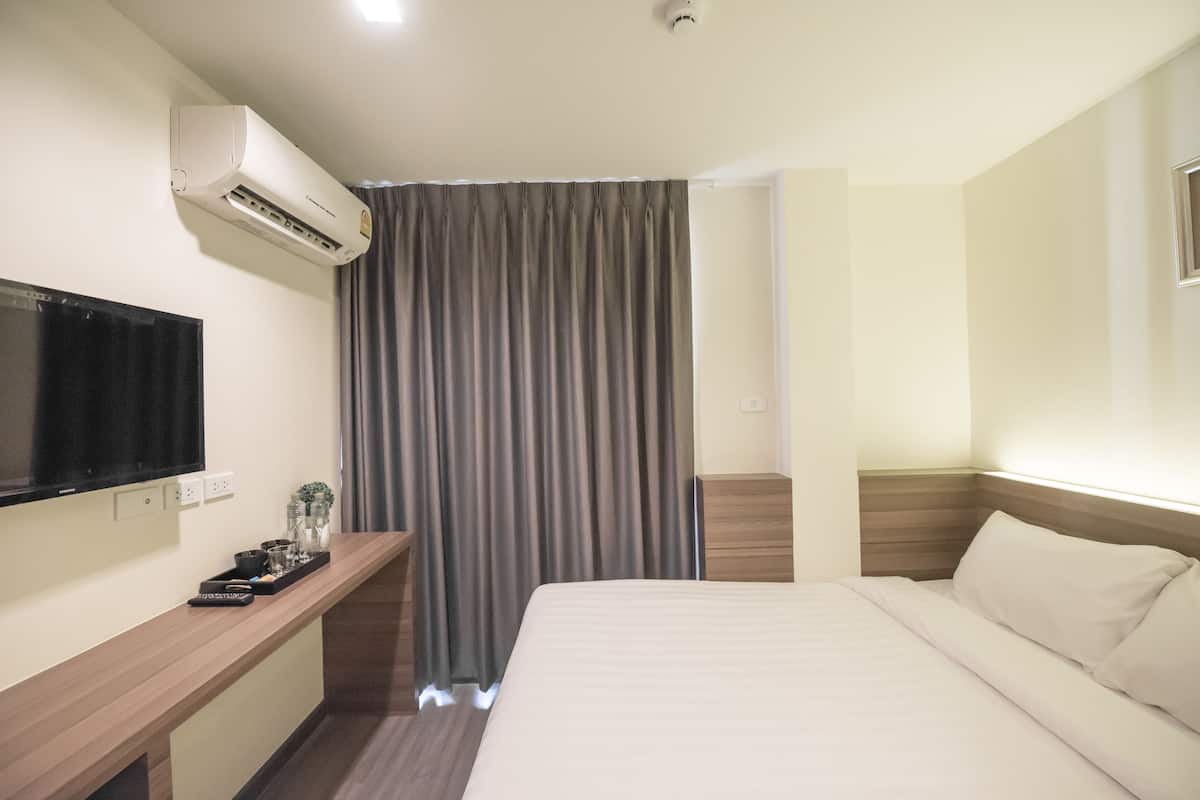 Habitación de hotel con cama, televisión, escritorio y control remoto, además de un equipo de aire acondicionado.