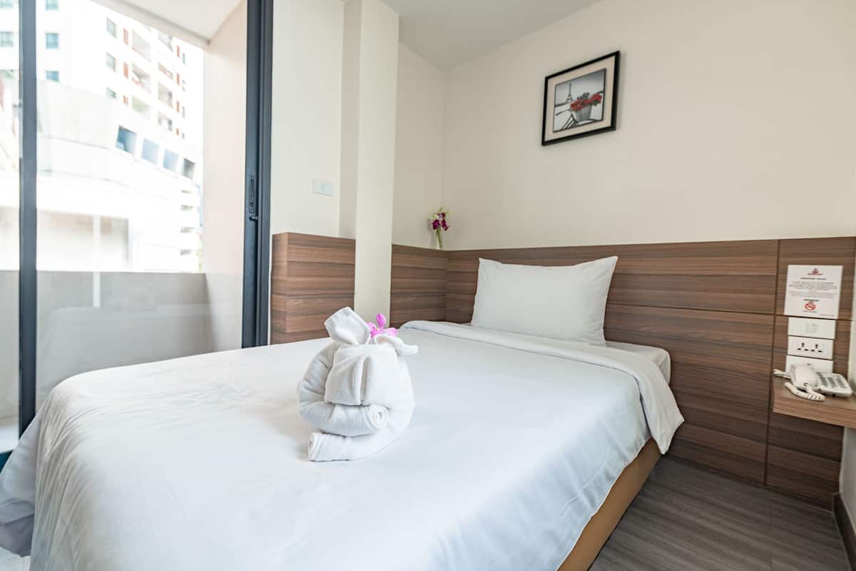 Habitación de hotel con una cama bien hecha, cabecera de madera, teléfono en la mesita de noche y un cuadro en la pared.