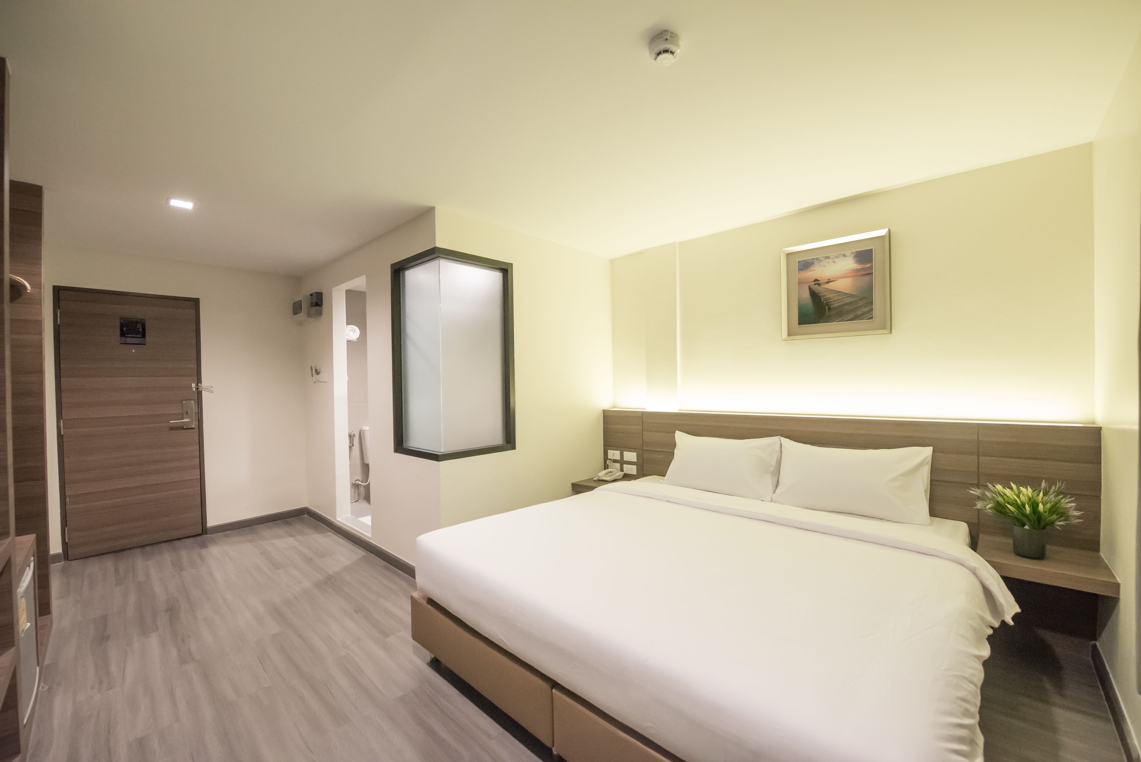 Une chambre d’hôtel avec un grand lit, une table de chevet avec une lampe, un téléviseur fixé au mur et une porte donnant sur une autre pièce.