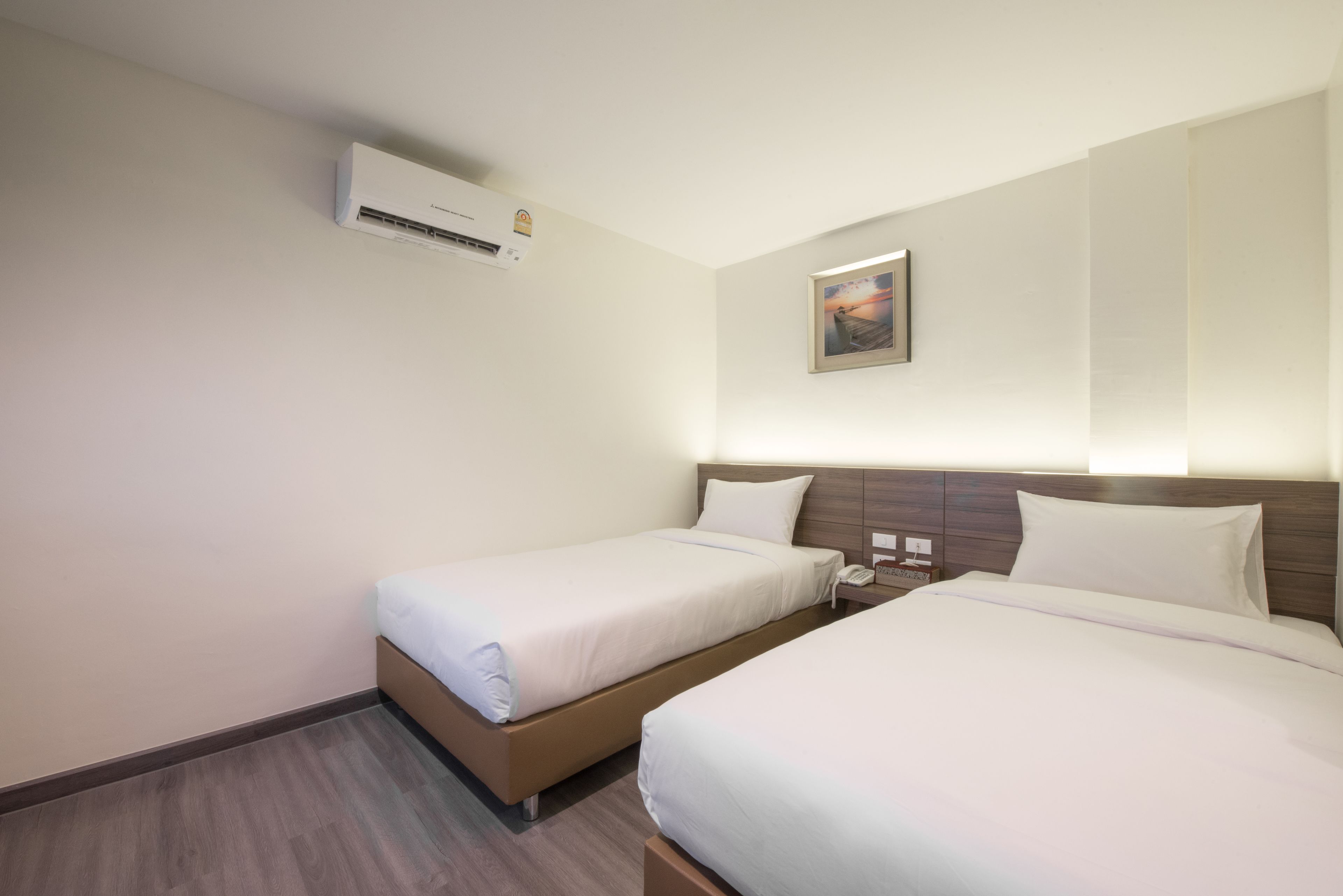 Habitación de hotel con dos camas individuales, una mesita de noche con teléfono y lámpara, y un cuadro en la pared.