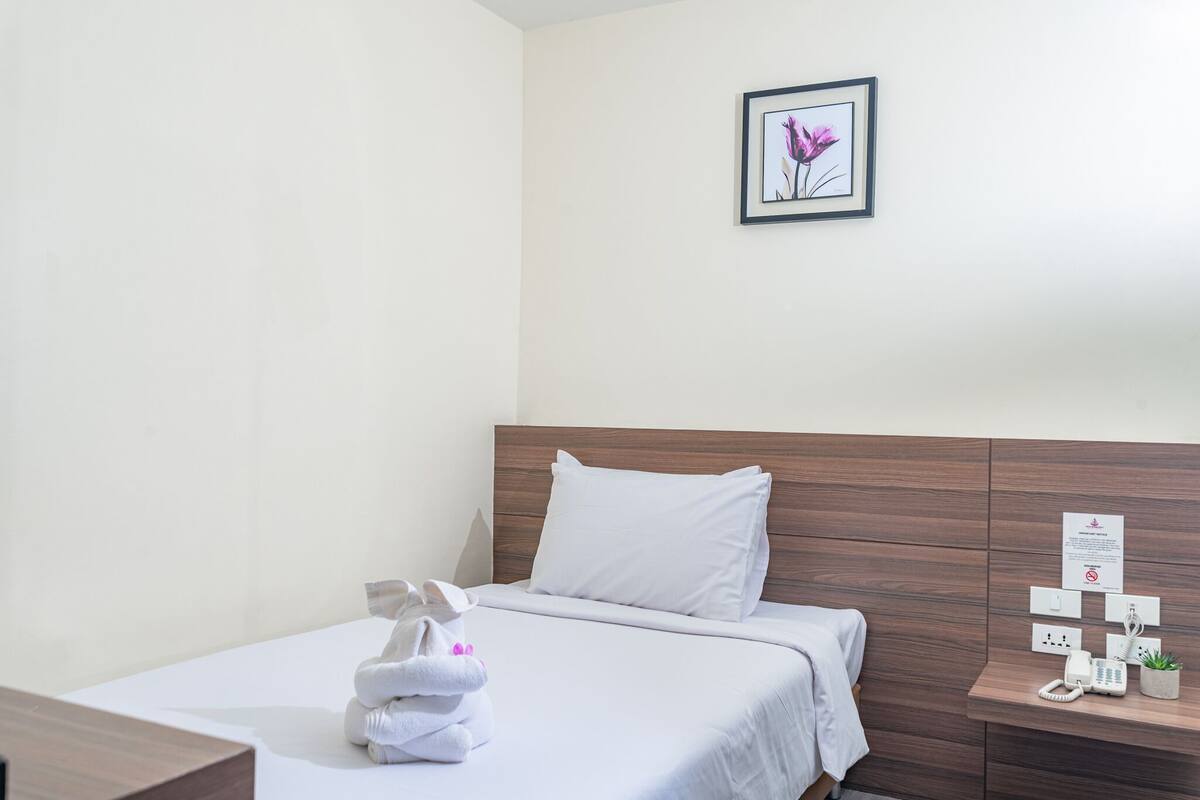 Habitación de hotel con una cama bien hecha, una mesita de noche con un teléfono y una planta pequeña, y un cuadro en la pared.