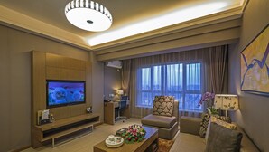 A modern living room with a flat-screen TV, a sofa, a coffee table, and a decorative plant. - Jinjiang Peninsula Seasons Hotel (Qinhuangdao)