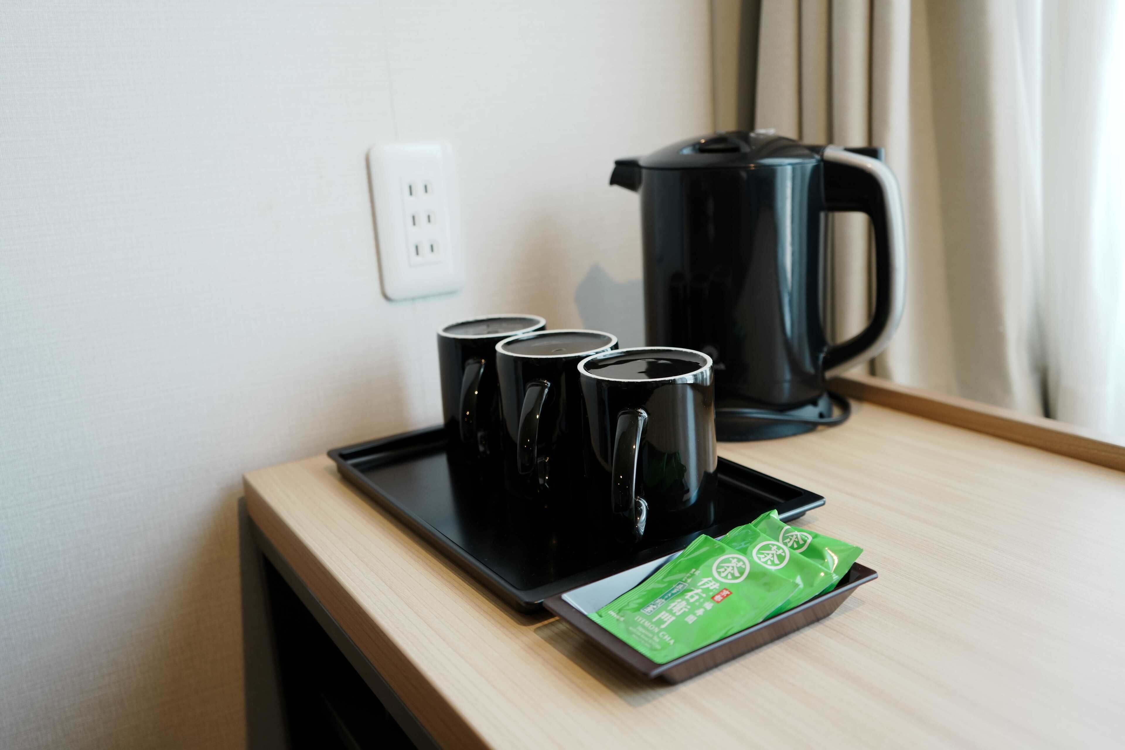 A tray with four black mugs and a green packet of tea on a wooden table.