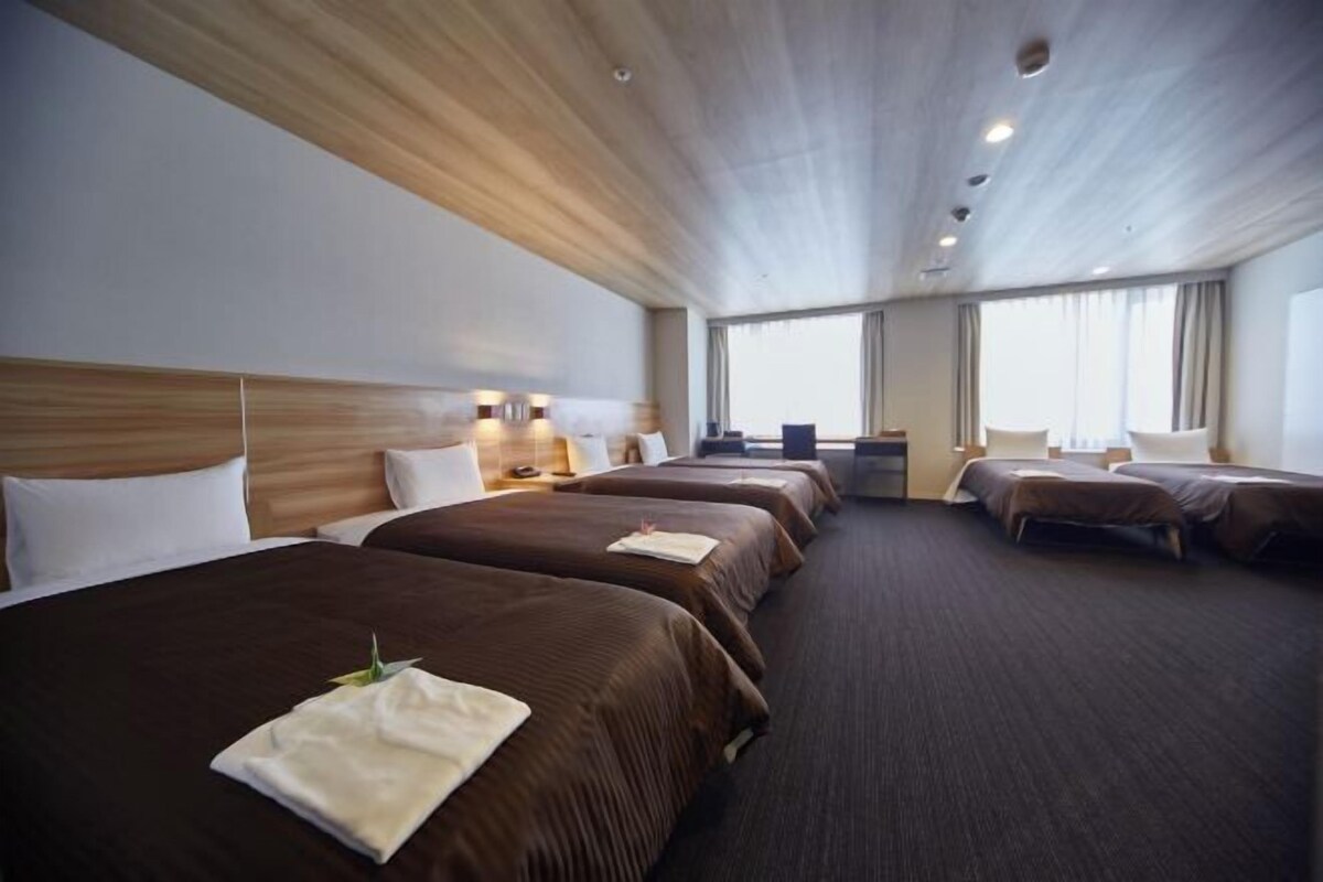 A hotel room with four beds arranged in a row, a wooden ceiling, and large windows.