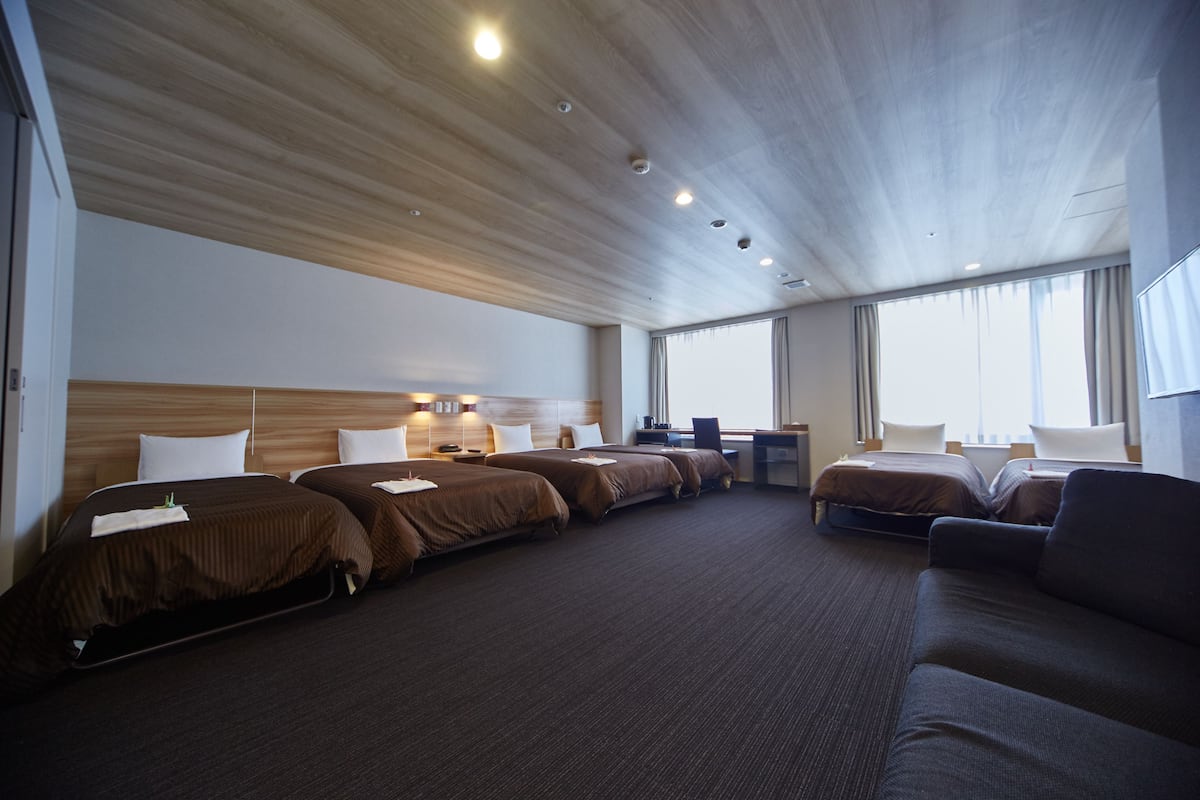 A hotel room with four beds, a desk, and a sofa.