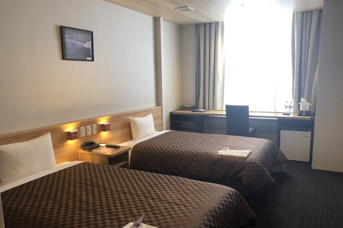 A hotel room with two beds, a desk, a chair, and a small refrigerator.