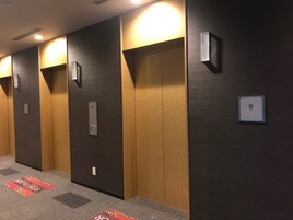 Un pasillo con tres ascensores, cada uno con su panel de control y una luz arriba.
