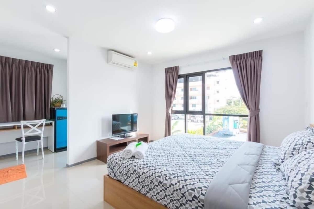 Habitación de hotel con cama, escritorio con computadora, televisor y ventana con cortinas.