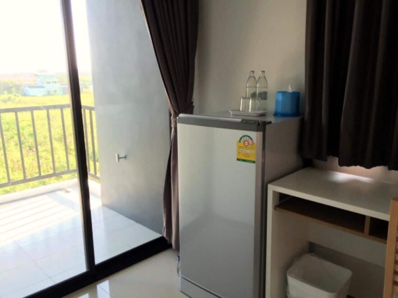A compact room with a balcony, a small refrigerator, a shelf with bottles, and a trash bin.