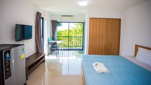 A hotel room with a bed, a TV, a desk with a chair, and a balcony with a table and chairs. - Promsook Apartment (Chonburi)