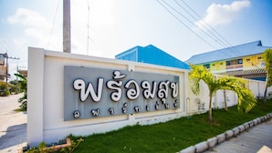 A sign with Thai script, a blue building, and a palm tree in front. - Promsook Apartment (Chonburi)
