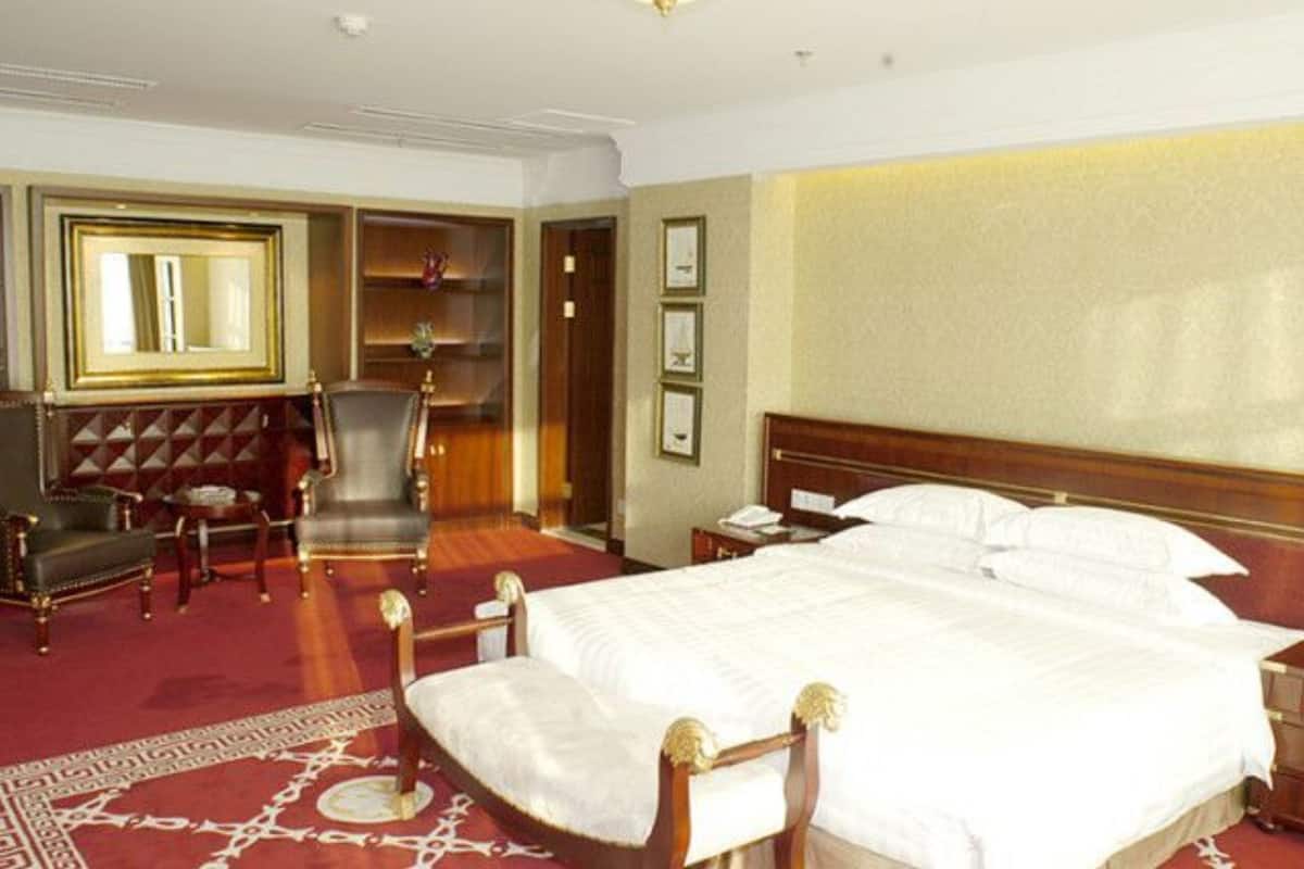 A hotel room with a large bed, a wooden headboard, a red carpet, a chair, a nightstand, and a mirror.