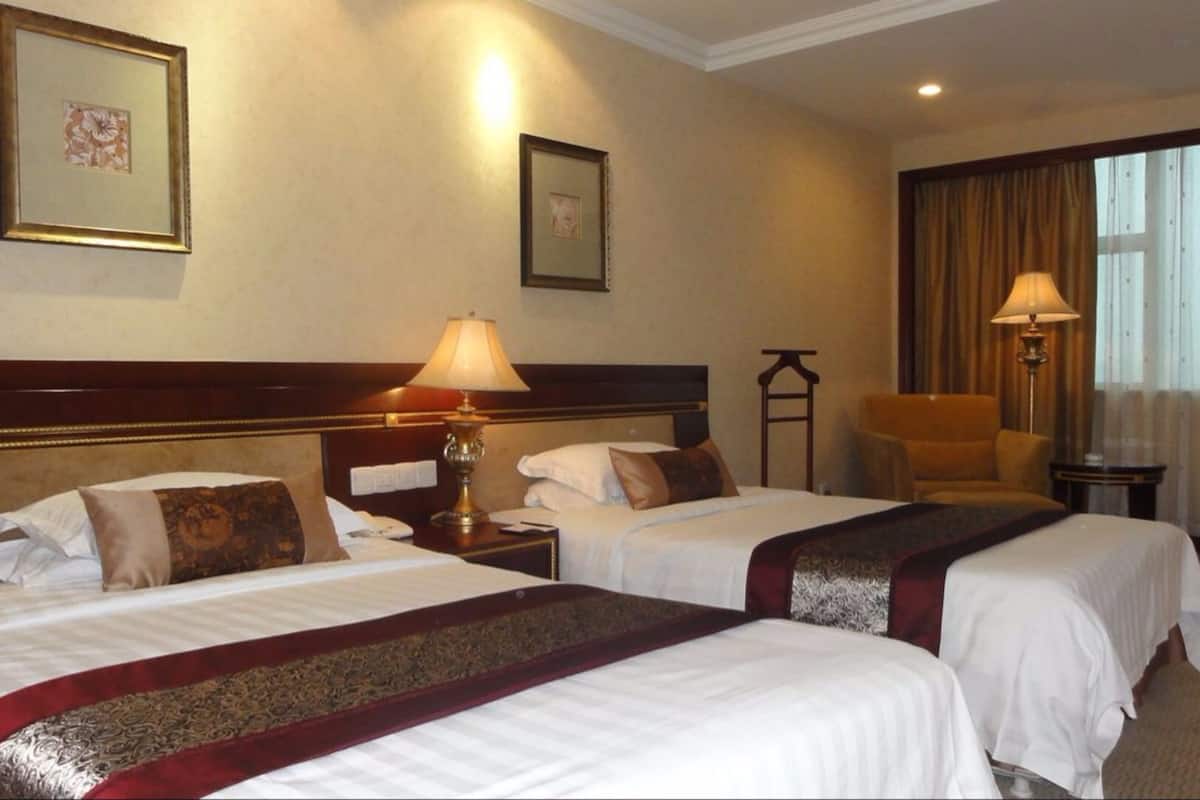 A hotel room with two beds, a nightstand with a lamp, a chair, and a desk.