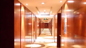 Un largo pasillo bien iluminado con alfombra estampada y paredes espejadas, que conduce a una puerta al final.