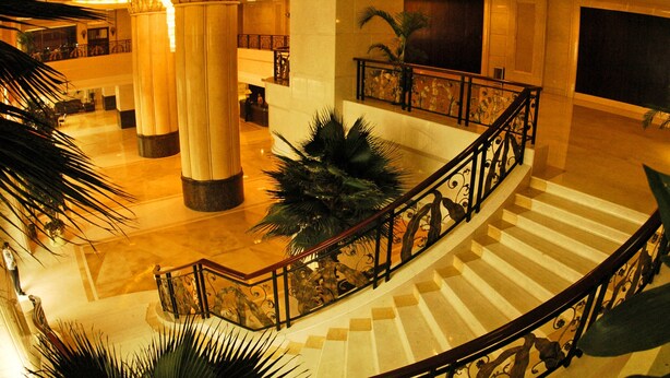 Un vestíbulo amplio con una imponente escalera, grandes columnas y barandales decorativos.