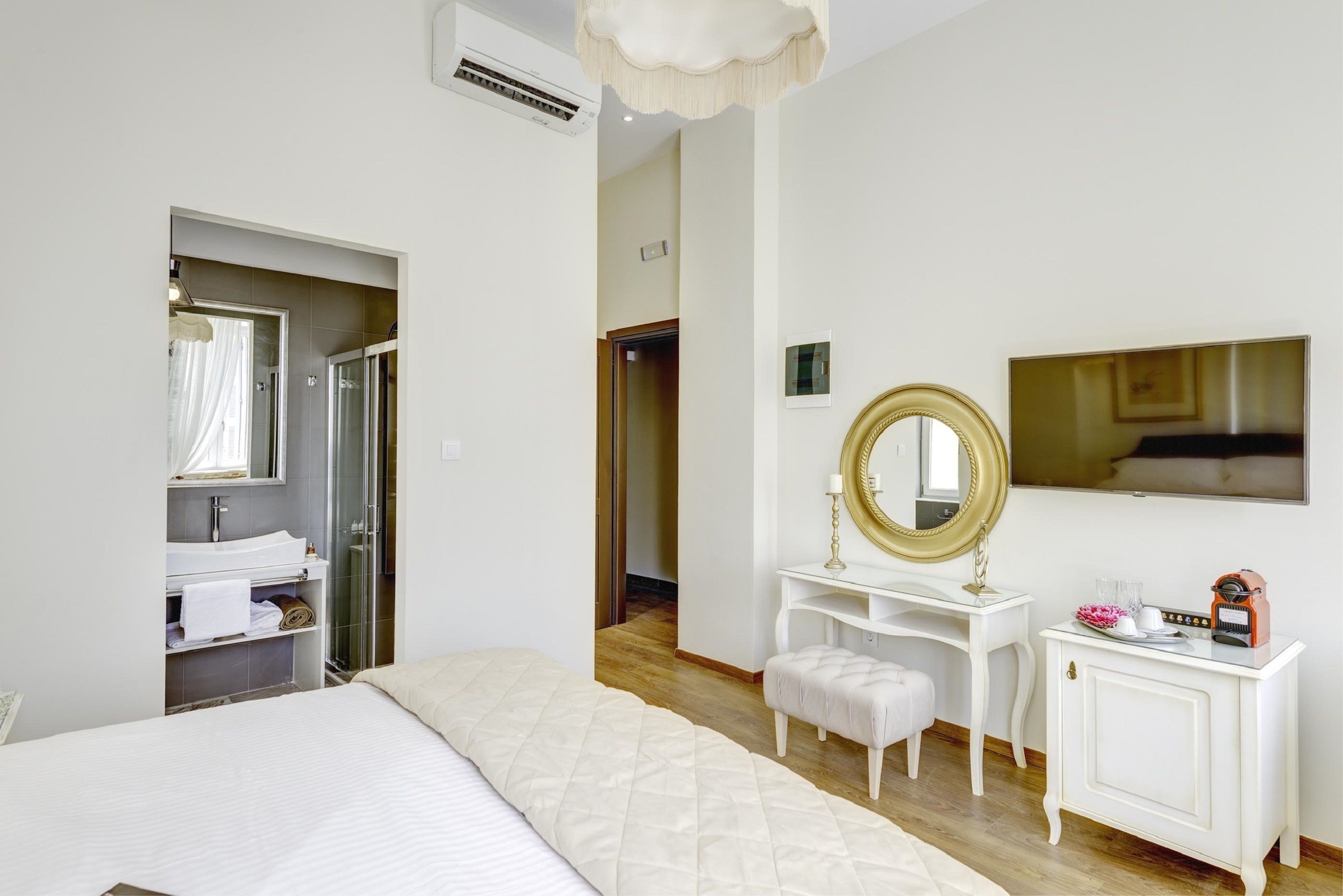 A bedroom with a bed, a vanity with a mirror, a dresser, and a television.