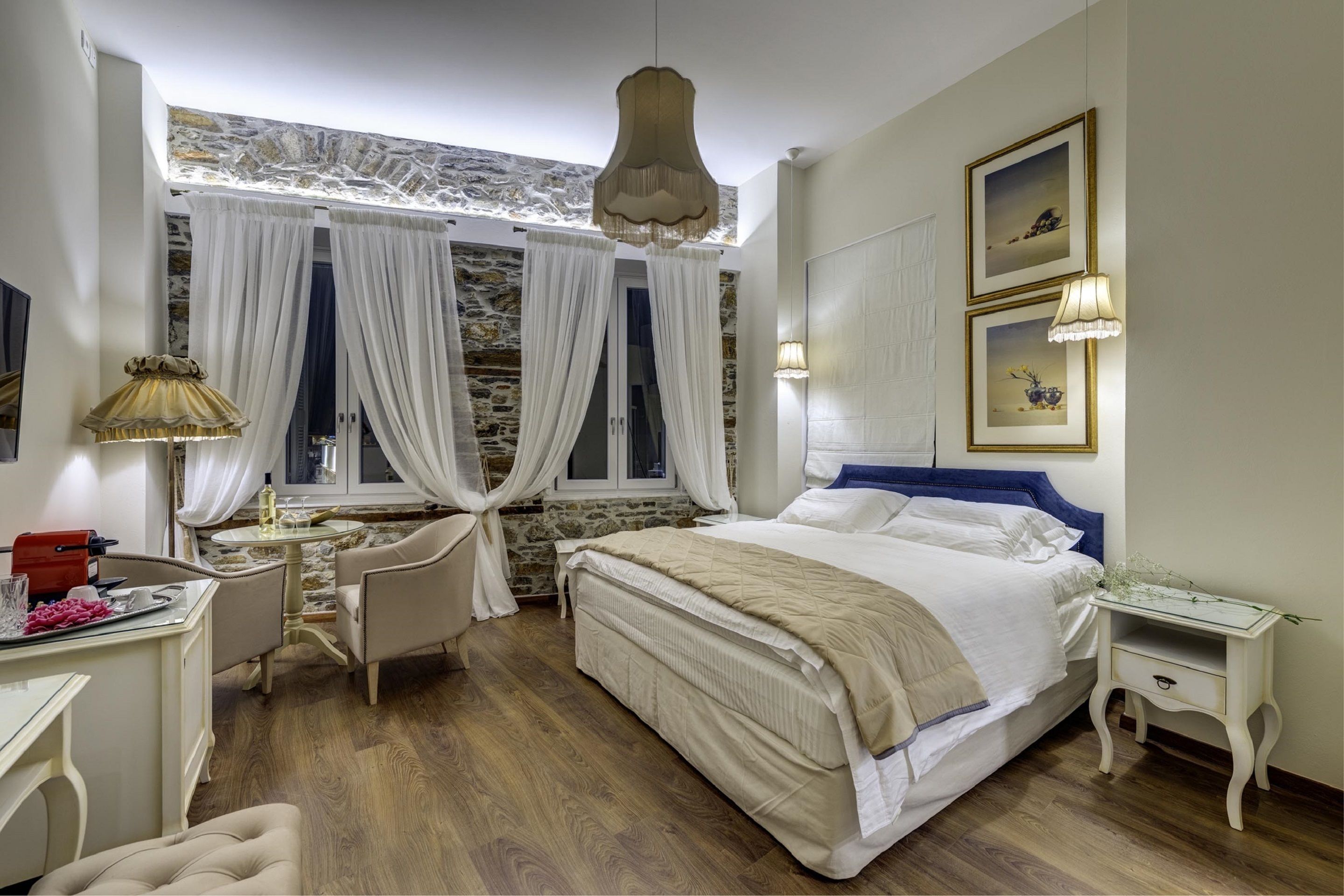 A bedroom with a large bed, a desk, and a chair. There are curtains on the windows, and a lamp on the desk.