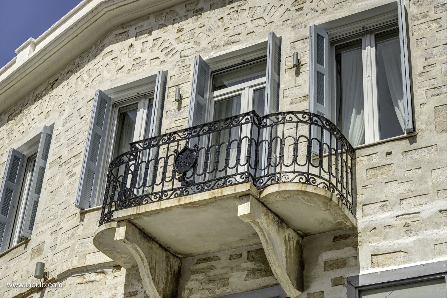 Een stenen gebouw met een balkon, voorzien van smeedijzeren hekken en luiken.