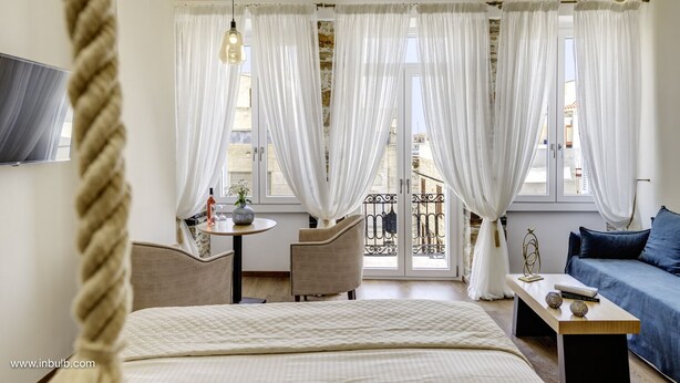 A hotel room with a bed, a sofa, a small table, and a balcony view. - 1844 Suites Syros (Syros)