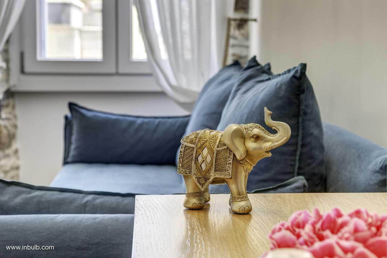 A living room with a sofa, a decorative elephant figurine on a table, and a window with curtains.