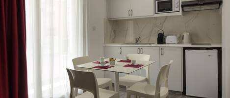 A modern kitchen with white cabinets, a microwave, a kettle, and a small refrigerator.