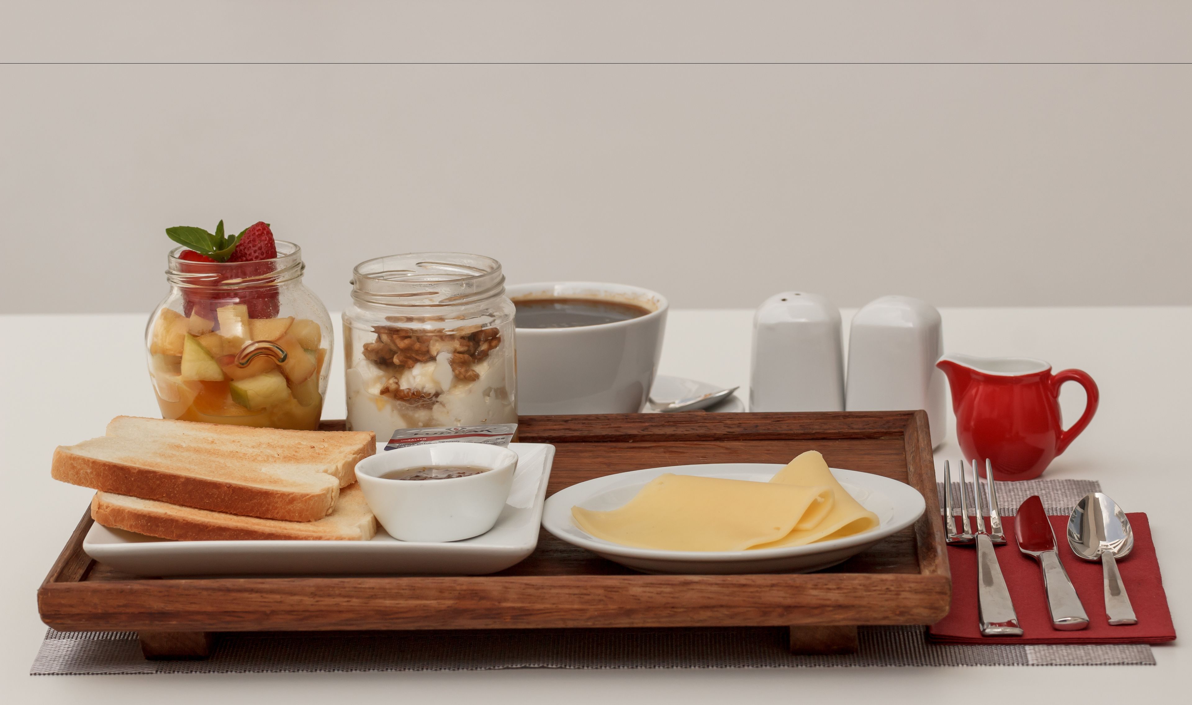 En frukostbricka med rostat bröd, frukt, yoghurt, ost och en kopp kaffe.
