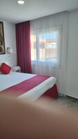 Habitación de hotel con una cama grande, una mesita de noche, una lámpara, una ventana con cortinas y un cuadro en la pared.