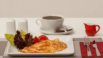 A breakfast setting with a plate of food, a cup of coffee, and a red pitcher.