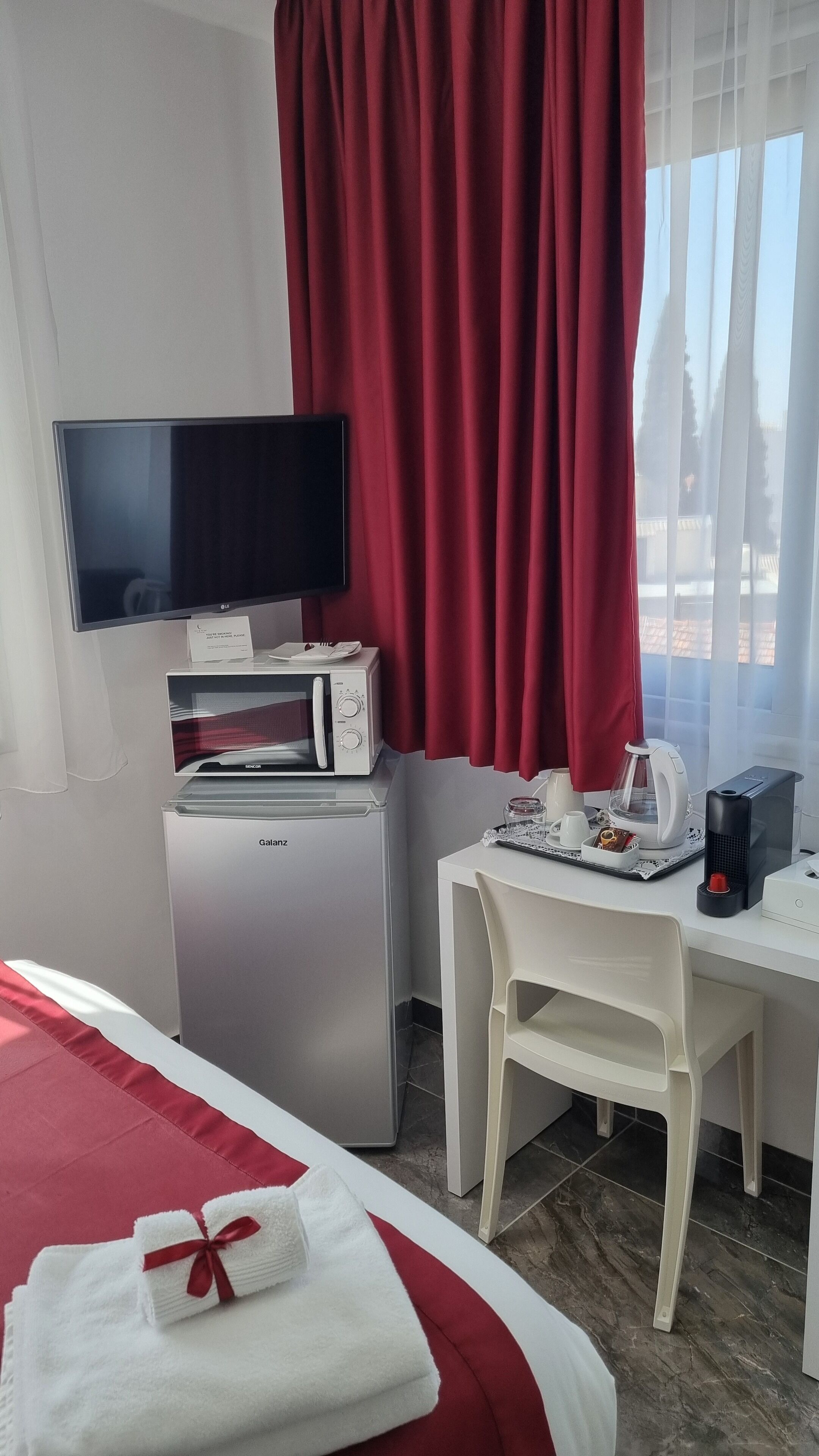 Hotellihuone, jossa on sänky, työpöytä tuolilla, mikroaaltouuni, vedenkeitin ja televisio.