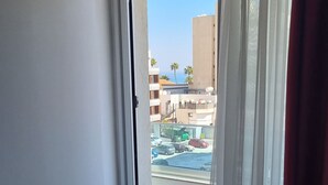 A room with a bed, a sliding glass door leading to a balcony, and a view of a parking area and buildings. - Art & Wine Boutique Hotel (Larnaca)