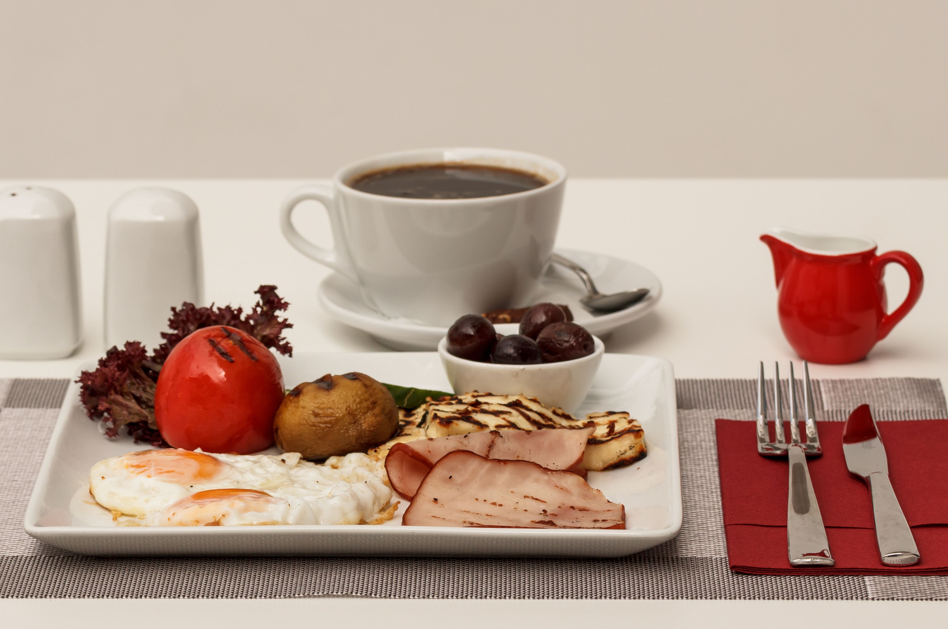 A breakfast plate with eggs, ham, a tomato, a muffin, and a cup of coffee.