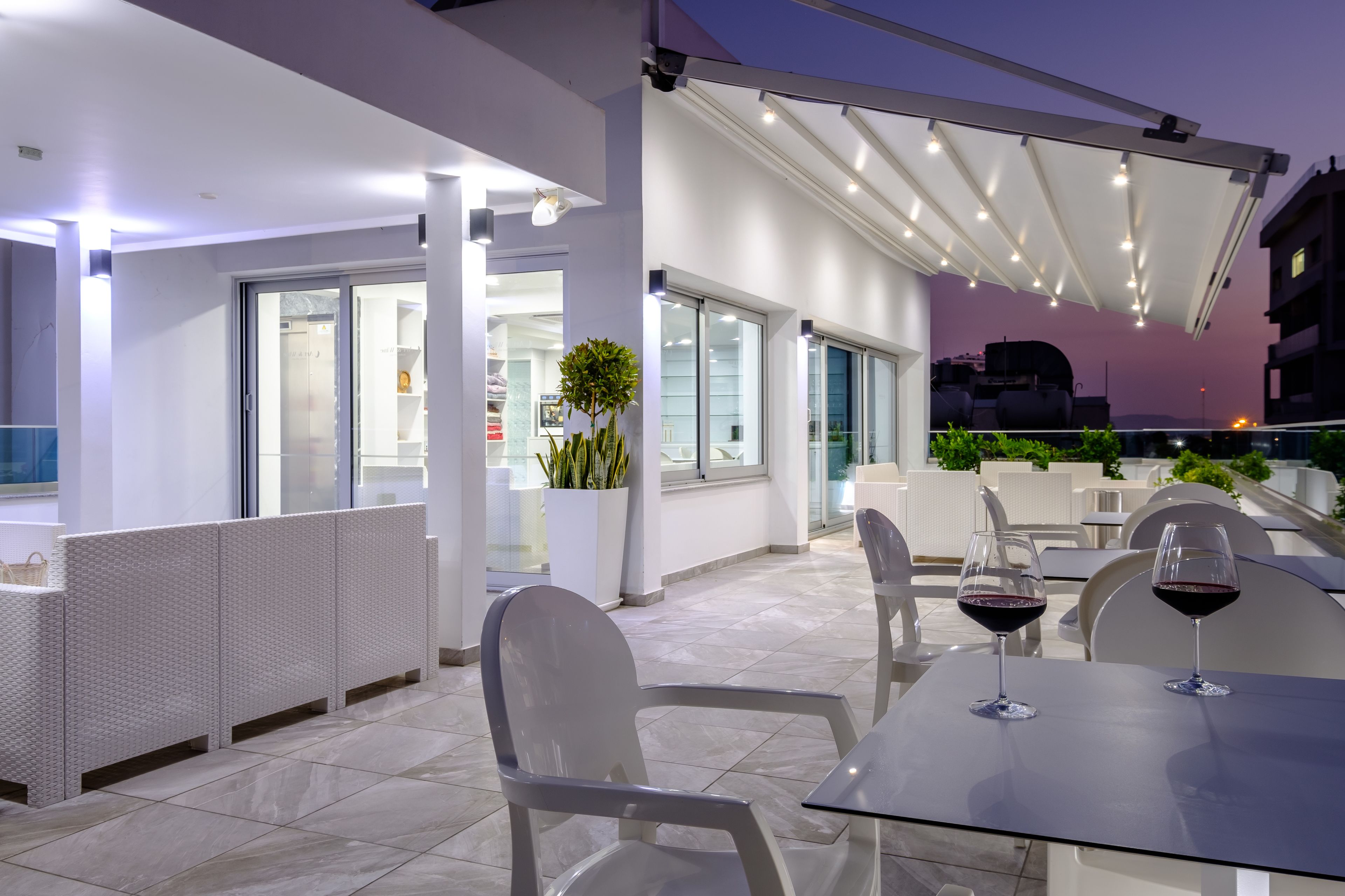 An outdoor patio area with seating and tables, a potted plant, and a view of the cityscape at dusk.