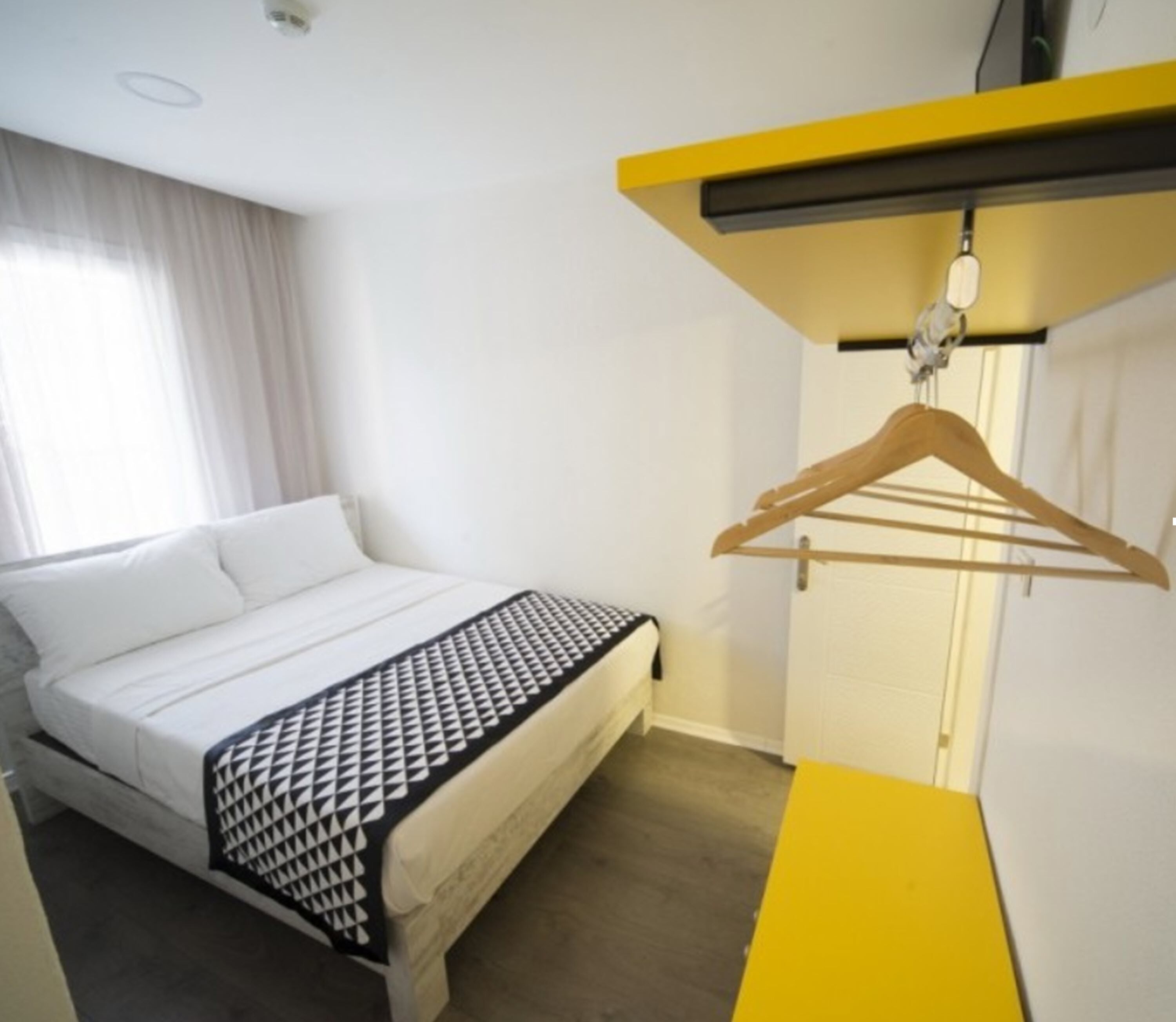 A hotel room with a bed, a hanging clothes rack, and a yellow desk.