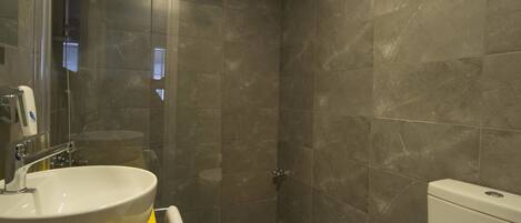Un baño moderno con un lavamanos amarillo, inodoro blanco y ducha con mampara de vidrio.