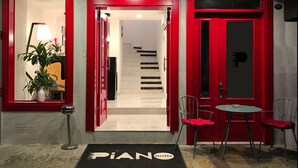 La entrada de un hotel con una puerta roja, una escalera que conduce al interior y un felpudo con la inscripción 'PIANO HOTEL'.