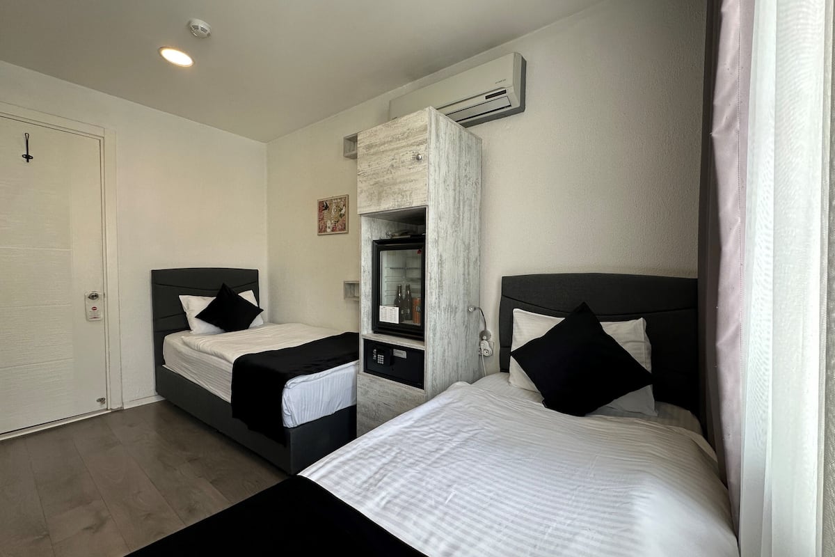A bedroom with two beds, a wardrobe, a mirror, and an air conditioning unit.