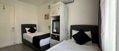 A bedroom with two beds, a wardrobe, a mirror, and an air conditioning unit.