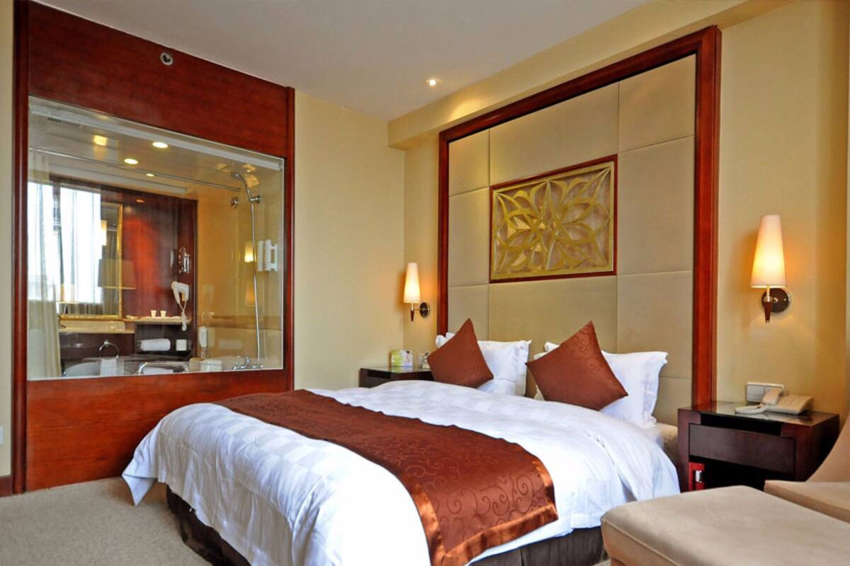 A hotel room with a large bed, a sitting area, a bathroom with a mirror, and a decorative wall panel.