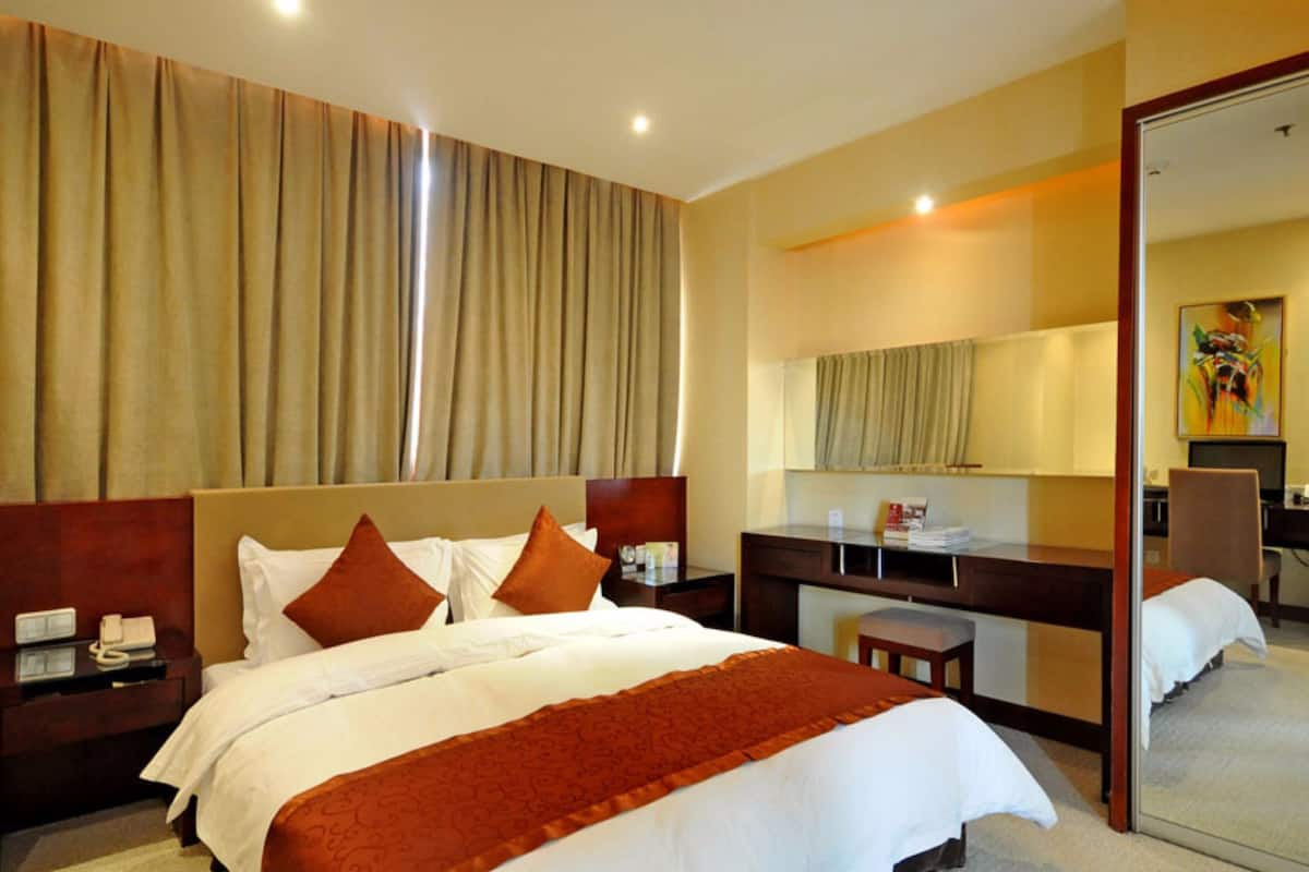 A hotel room with a large bed, a desk, a chair, a mirror, and a window with curtains.