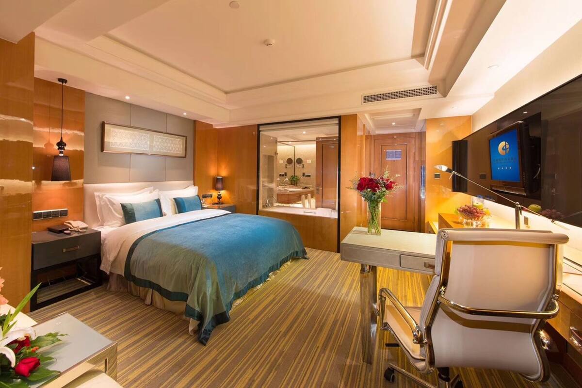 A hotel room with a bed, bedside table, lamp, and a TV.