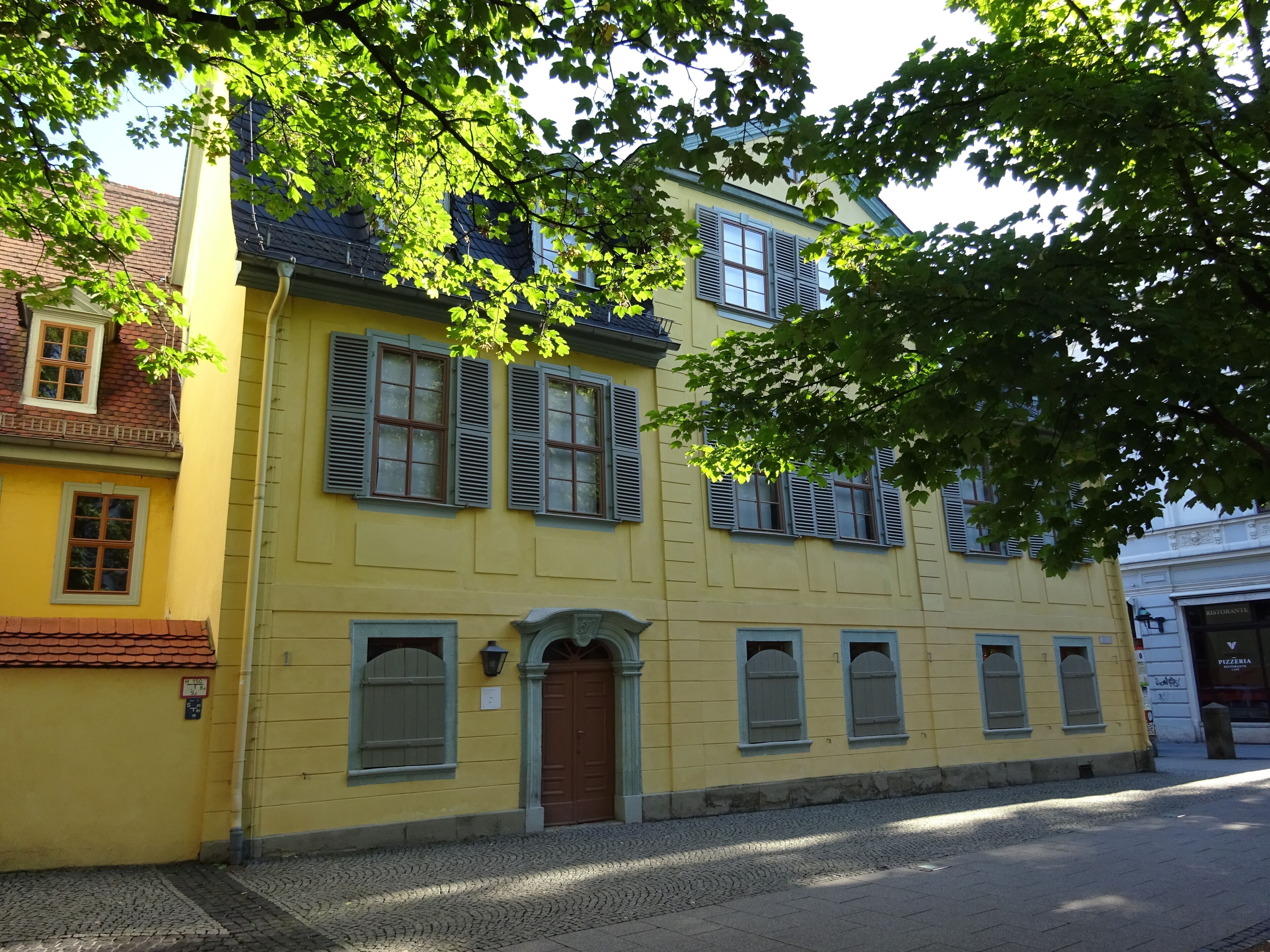 A yellow building with multiple windows and a brown door, surrounded by cobblestone pavement.