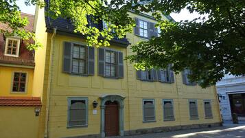 A yellow building with multiple windows and a brown door, surrounded by cobblestone pavement.