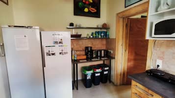 Cozinha equipada com geladeira, micro-ondas, cafeteira e lixeiras.