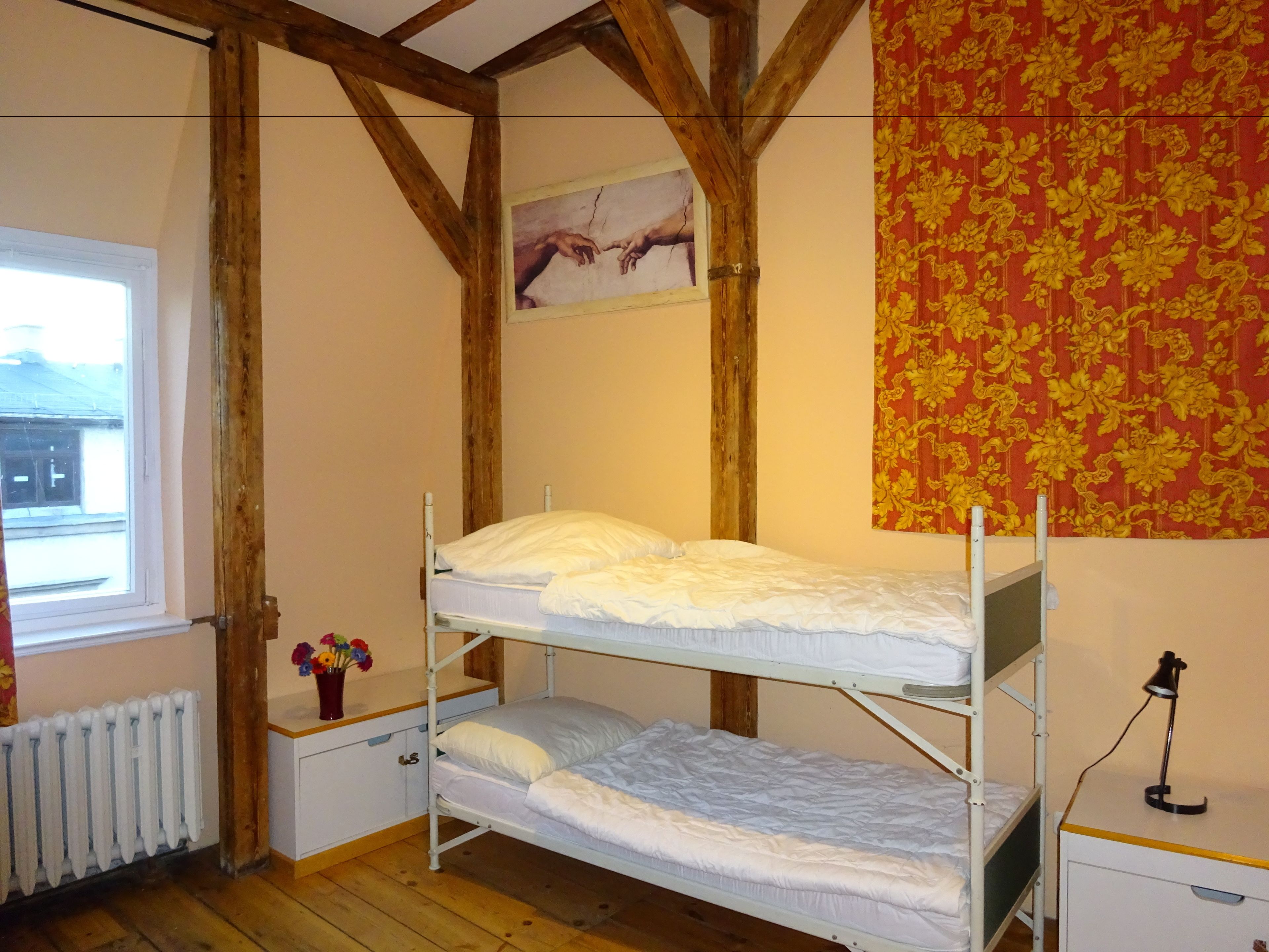 A dormitory room with two bunk beds, a radiator, a window, and a wall with a floral pattern.