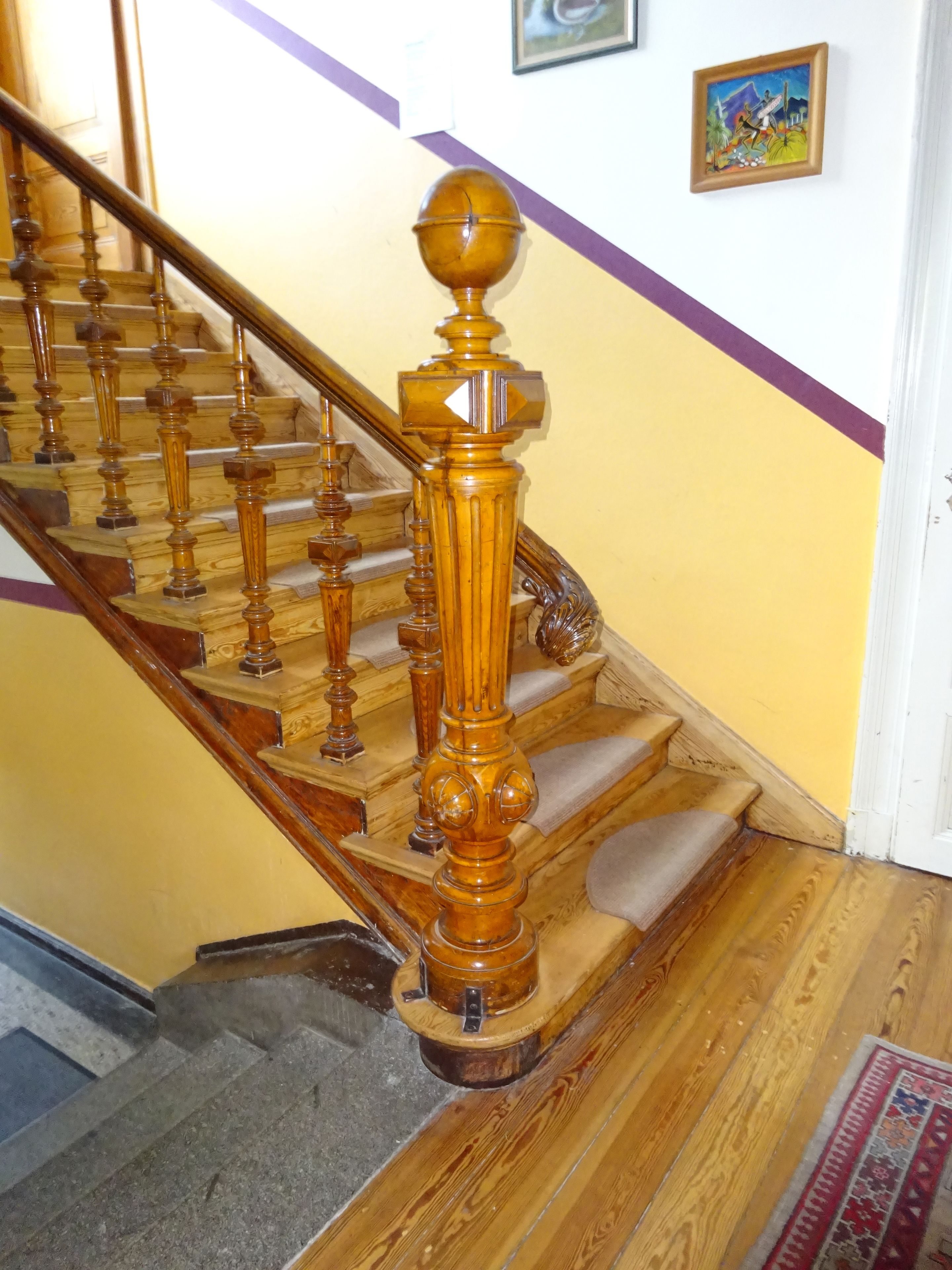 Una escalera de madera con barandilla y un tapete estampado al final.